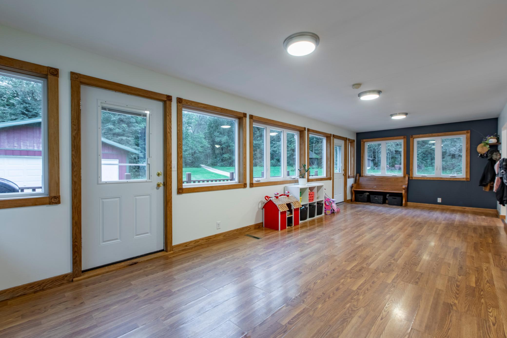 Bright room with wood-look floors, rows of wood-trimmed windows, and a bench and toy cubbies.