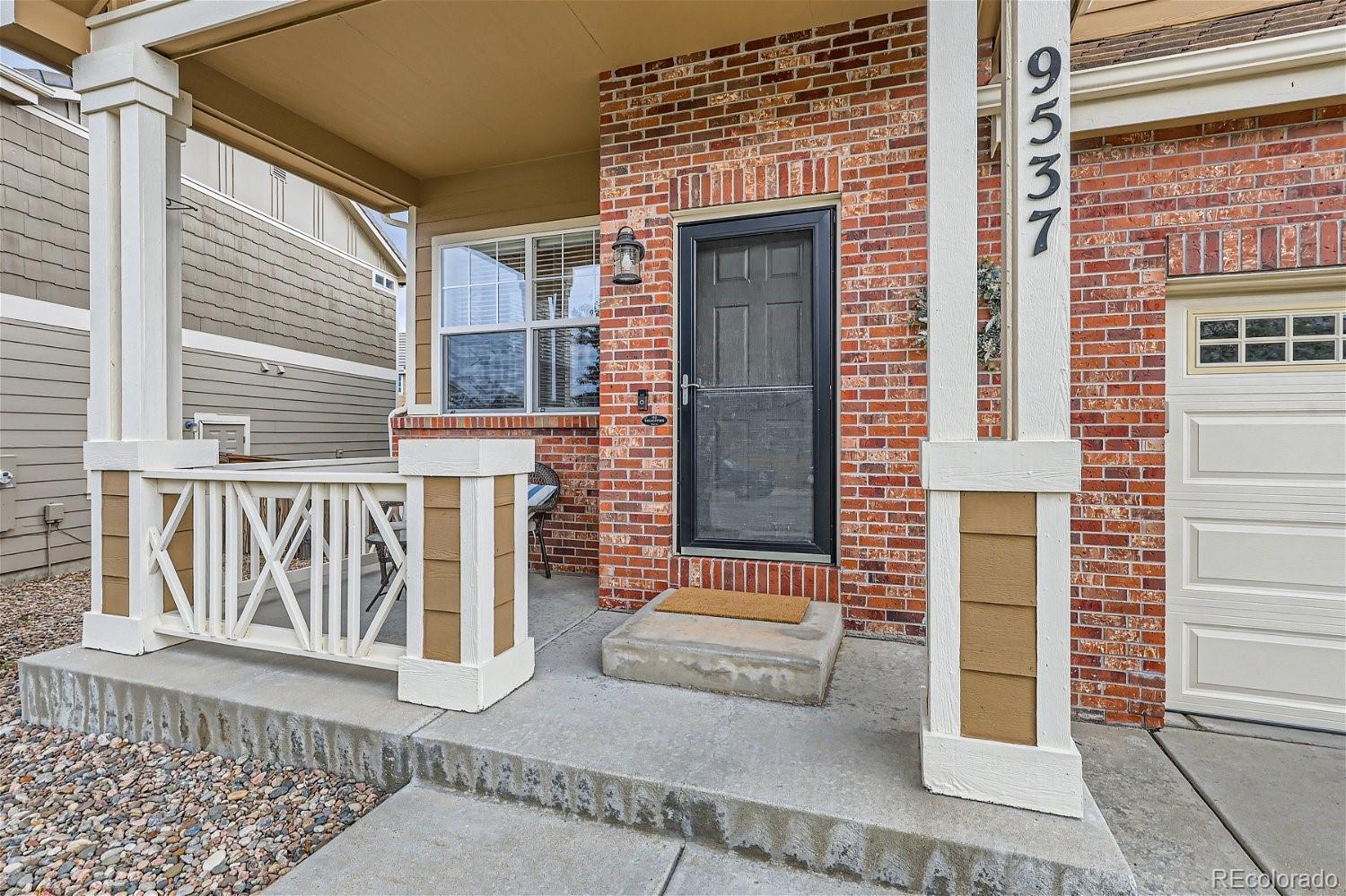 Brick house entry with covered porch, white railings, and address number 9537.