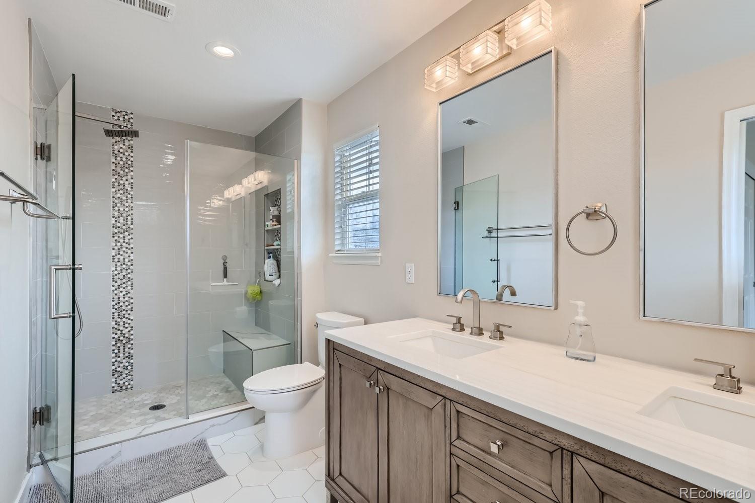Bathroom with a glass walk-in shower and long double vanity with gray cabinetry.