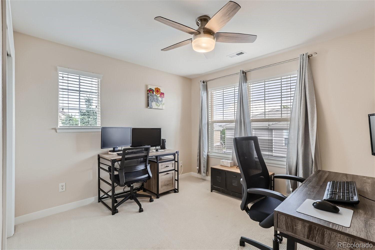 Home office with two computer desks, office chairs, and windows with blinds.