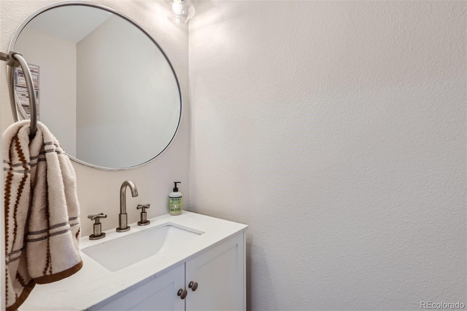 Bathroom vanity with a white sink, large round mirror, and striped towels.