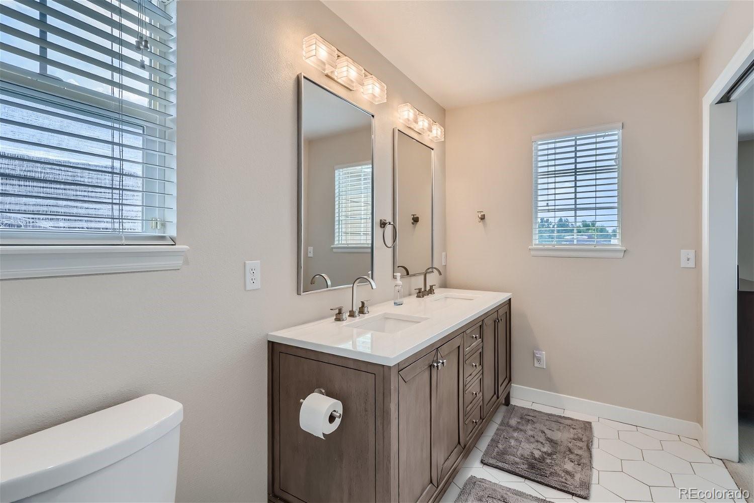Bathroom with a dark wood double vanity, two mirrors, and white hexagonal floor tile.