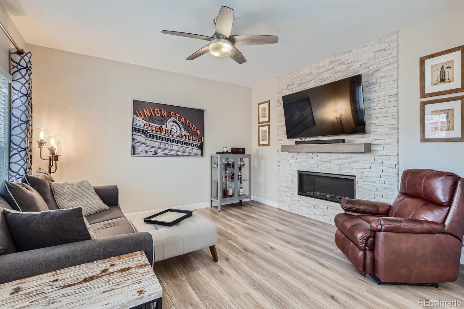 Living room with a white stone fireplace wall, mounted television, gray sectional, and leather recliner.
