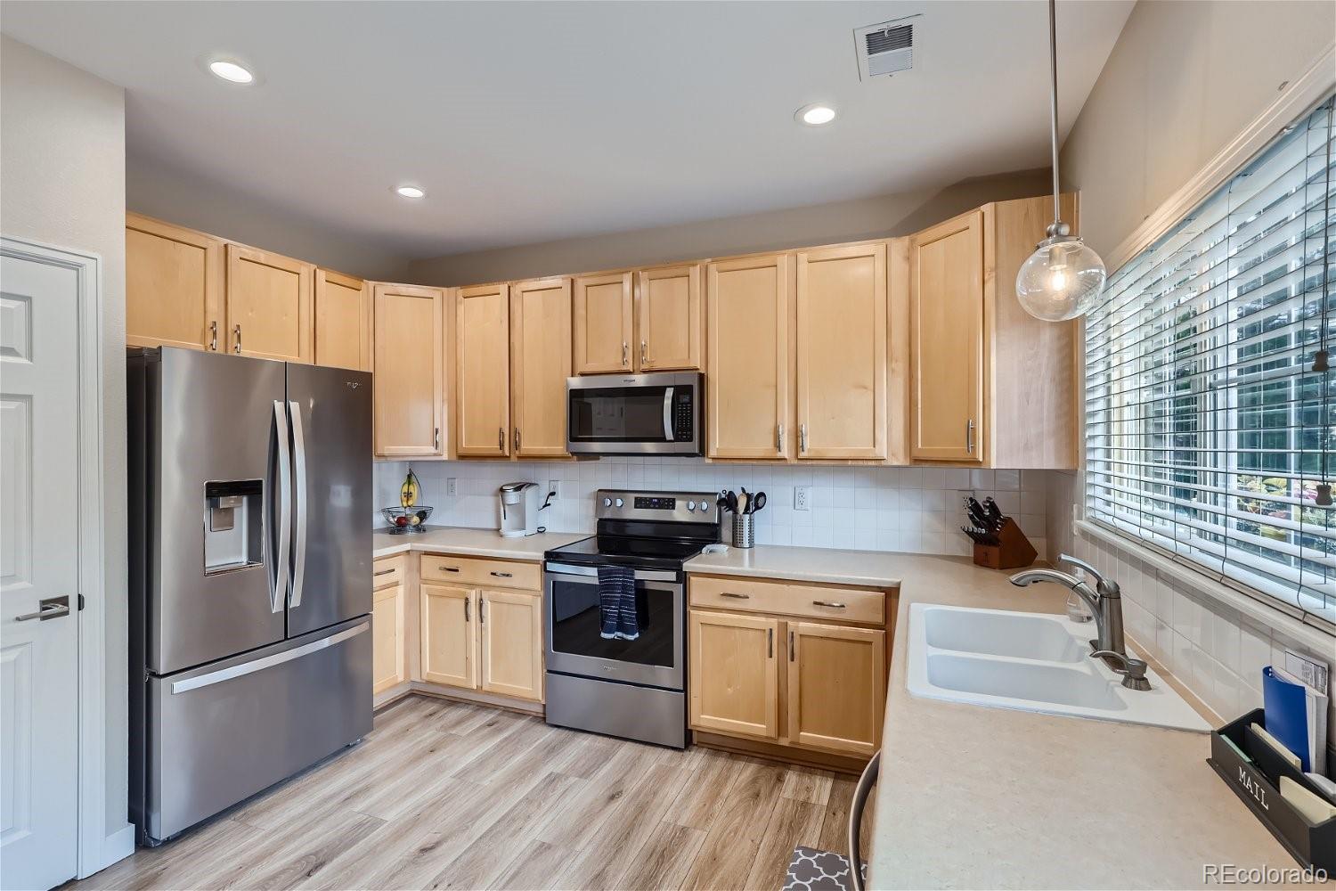Kitchen with light wood cabinets, stainless steel appliances, and a white farmhouse sink beneath a large window.