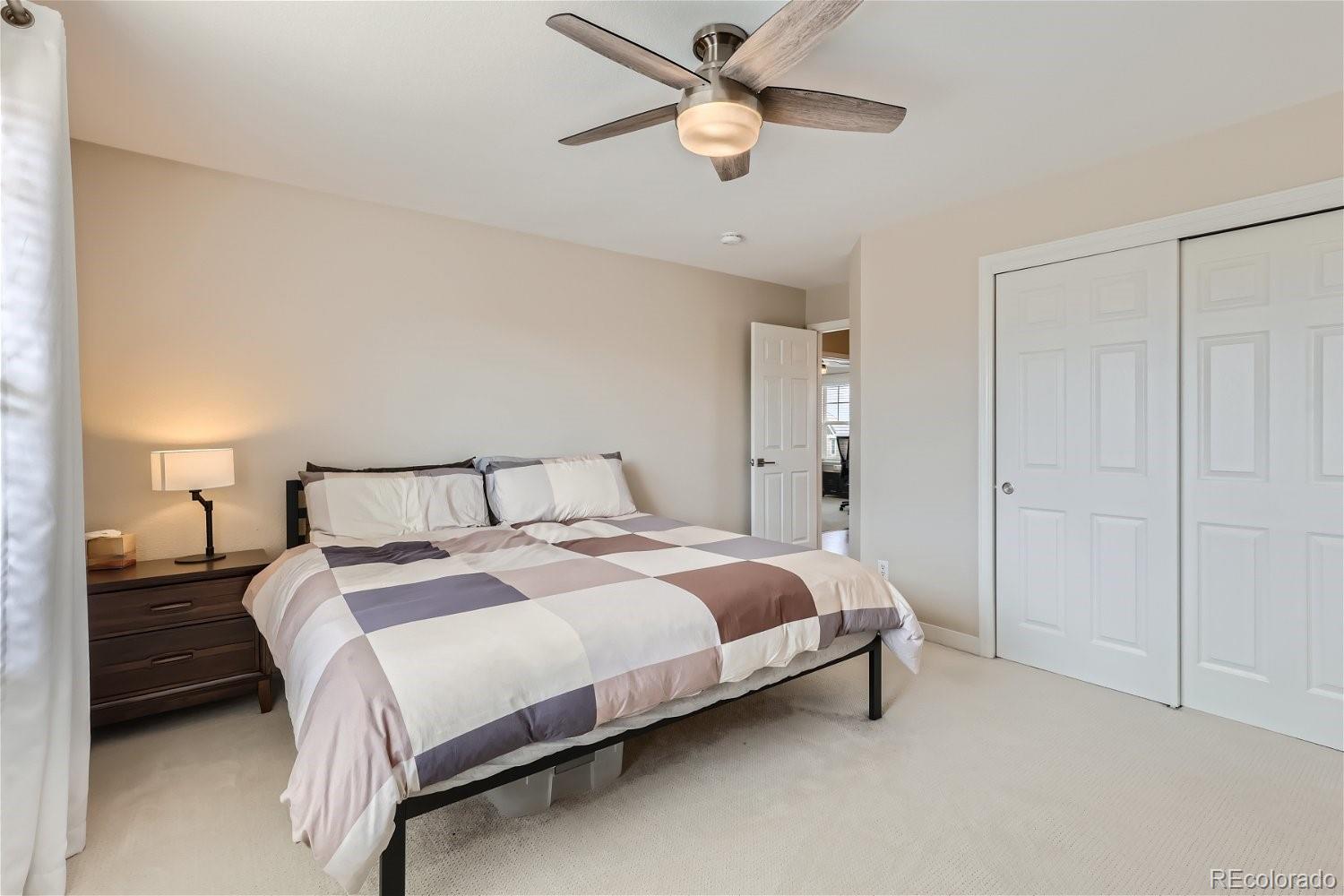 Bedroom with a block-pattern quilt, dark wood nightstand, ceiling fan, and white sliding closet doors.