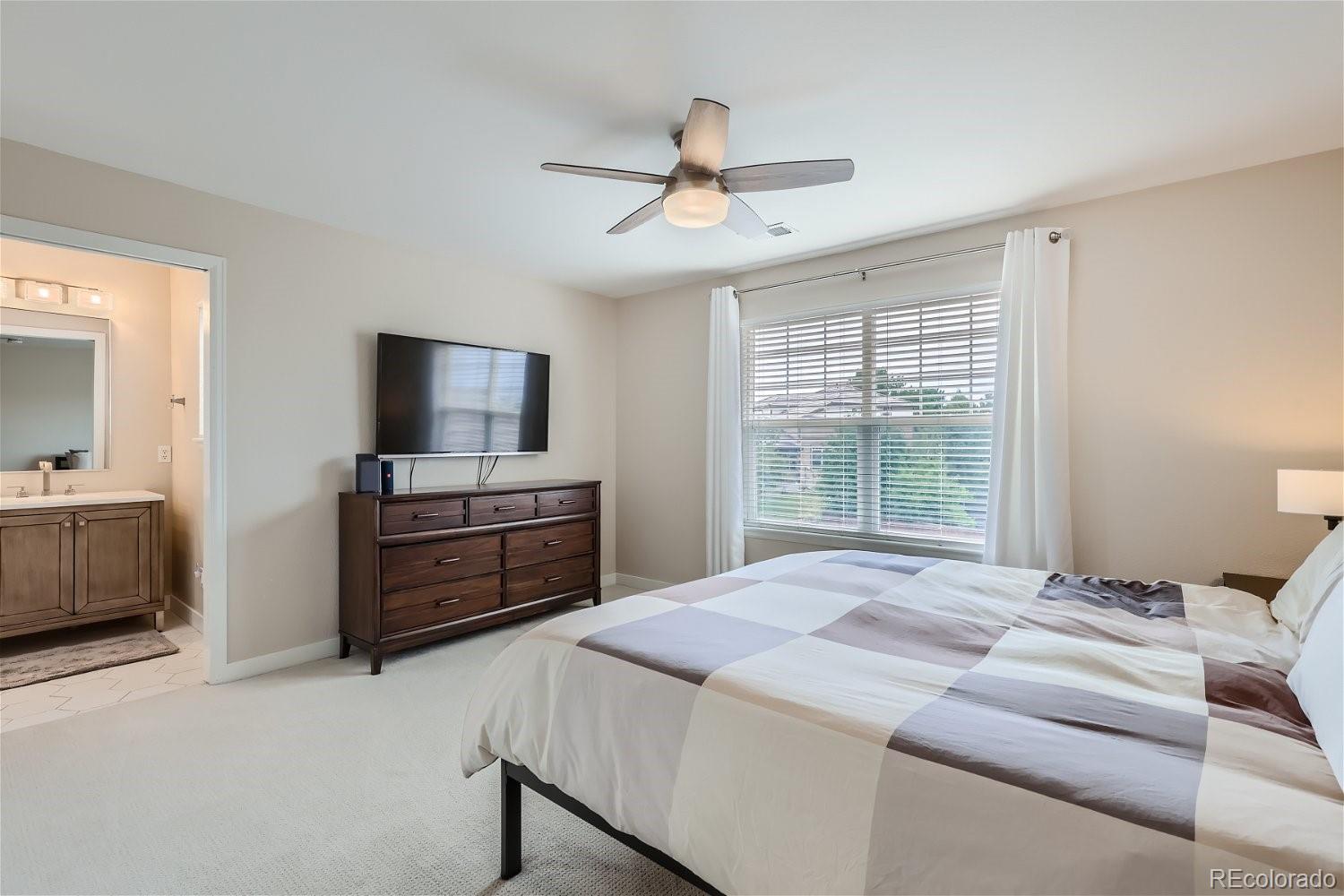 Bedroom with a patchwork bedspread, dark wood dresser, wall-mounted television, and adjoining bathroom doorway.