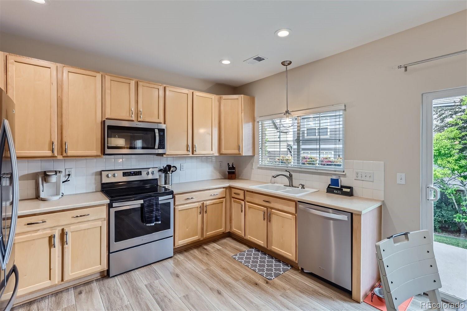 Kitchen with light wood cabinets, stainless steel appliances, and a corner sink beneath a window.