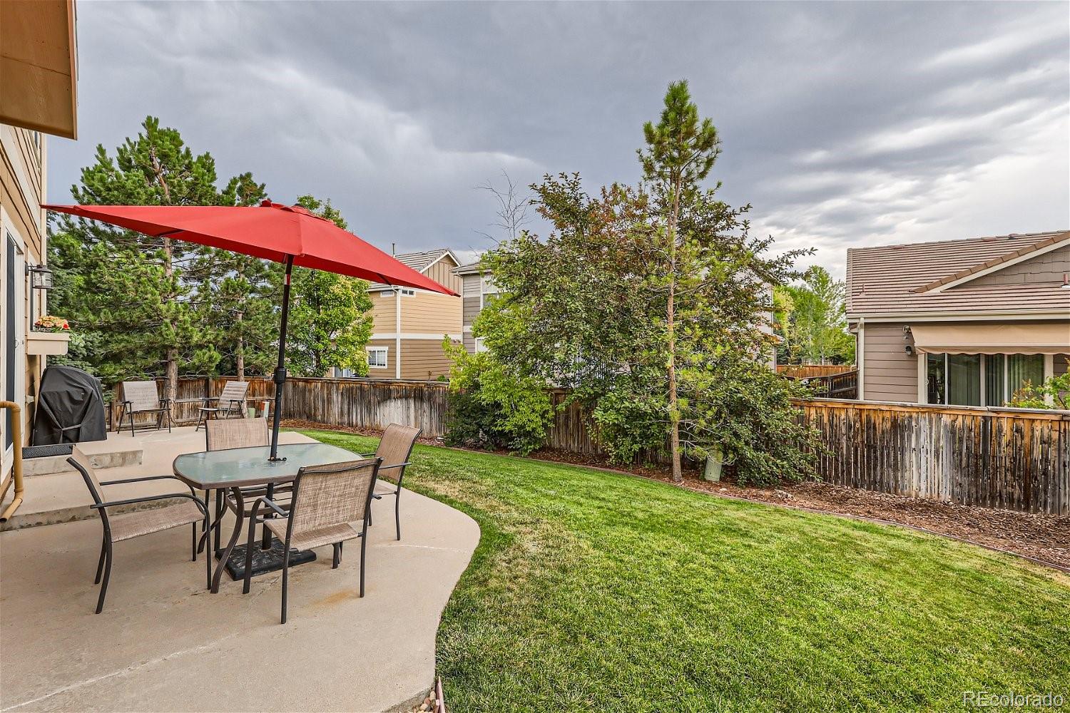 Fenced backyard with a furnished patio, red umbrella, and green lawn.