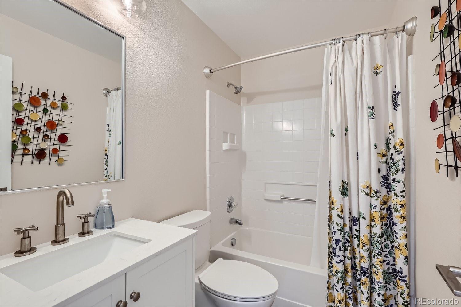 Bathroom with a white vanity, tub-shower combination, and floral shower curtain.