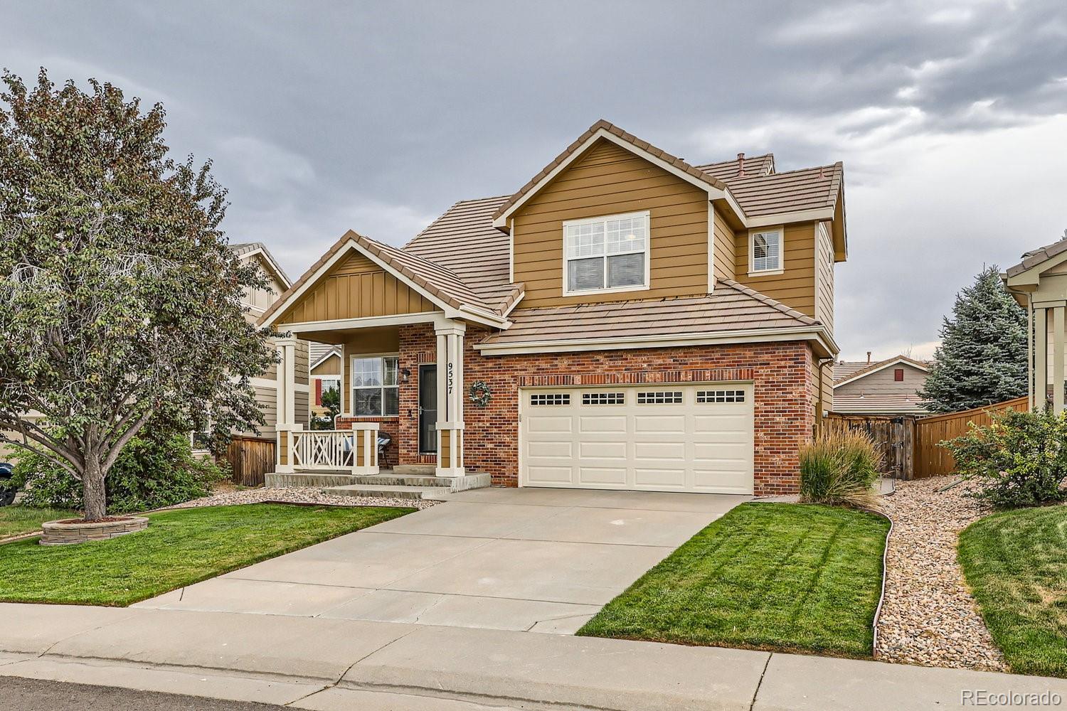 Two-story brown-and-brick house with a covered porch, two-car garage, and landscaped front yard.