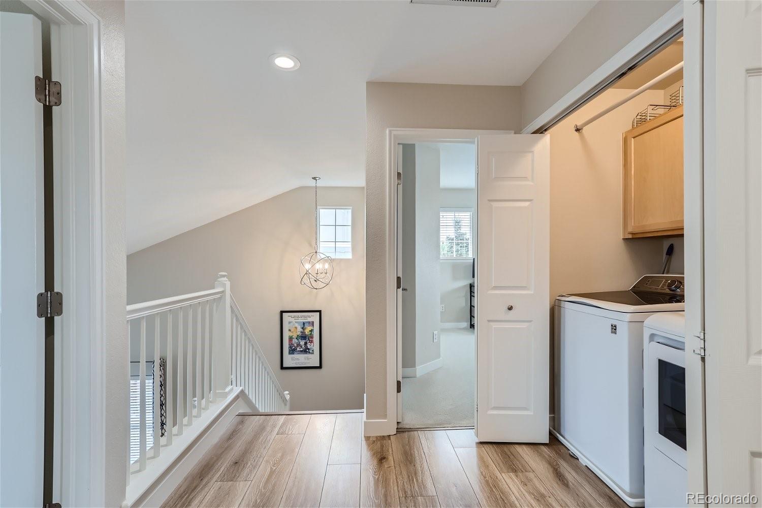 Upstairs landing with a stair railing beside an open laundry closet with washer and dryer.