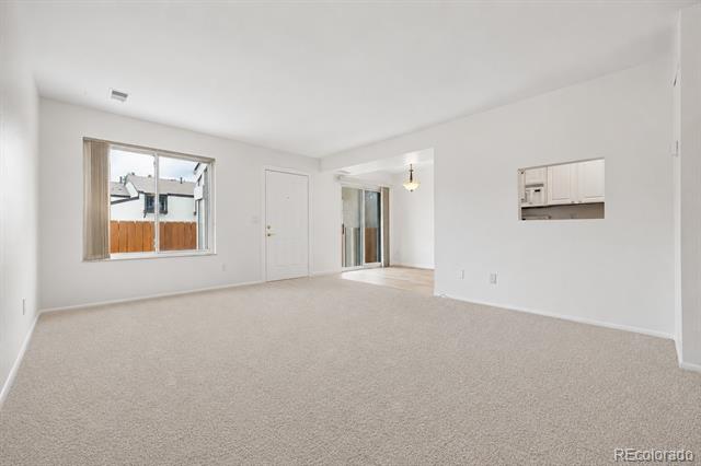 Empty living room with beige carpet, a window overlooking a fence, and a sliding glass door.