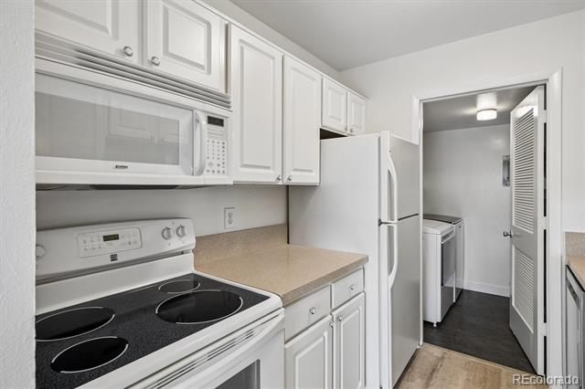 Kitchen with white cabinets and appliances, opening onto a laundry area.