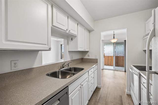 Kitchen with white cabinets, gray countertops, and a double-basin sink leading to sliding patio doors.