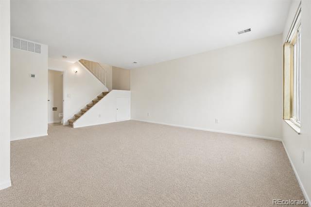 Empty living room with beige carpet, a staircase, and a tall window.