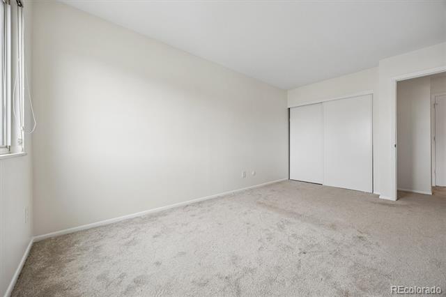Empty bedroom with beige carpet, a window with blinds, and sliding closet doors.