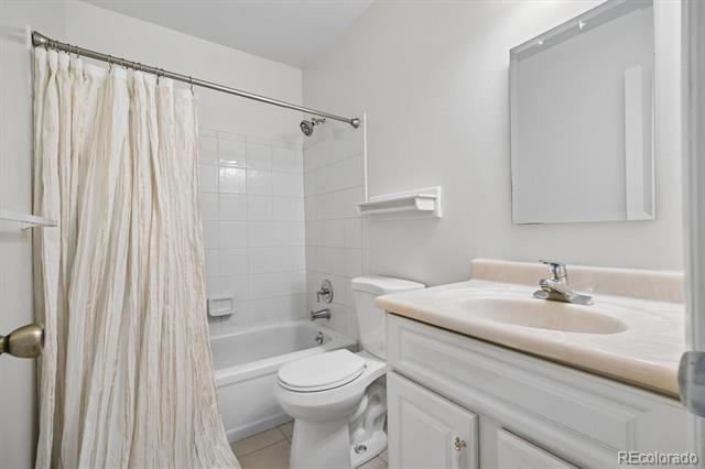 Bathroom with a tub-shower behind a curtain and a white vanity with an oval sink.