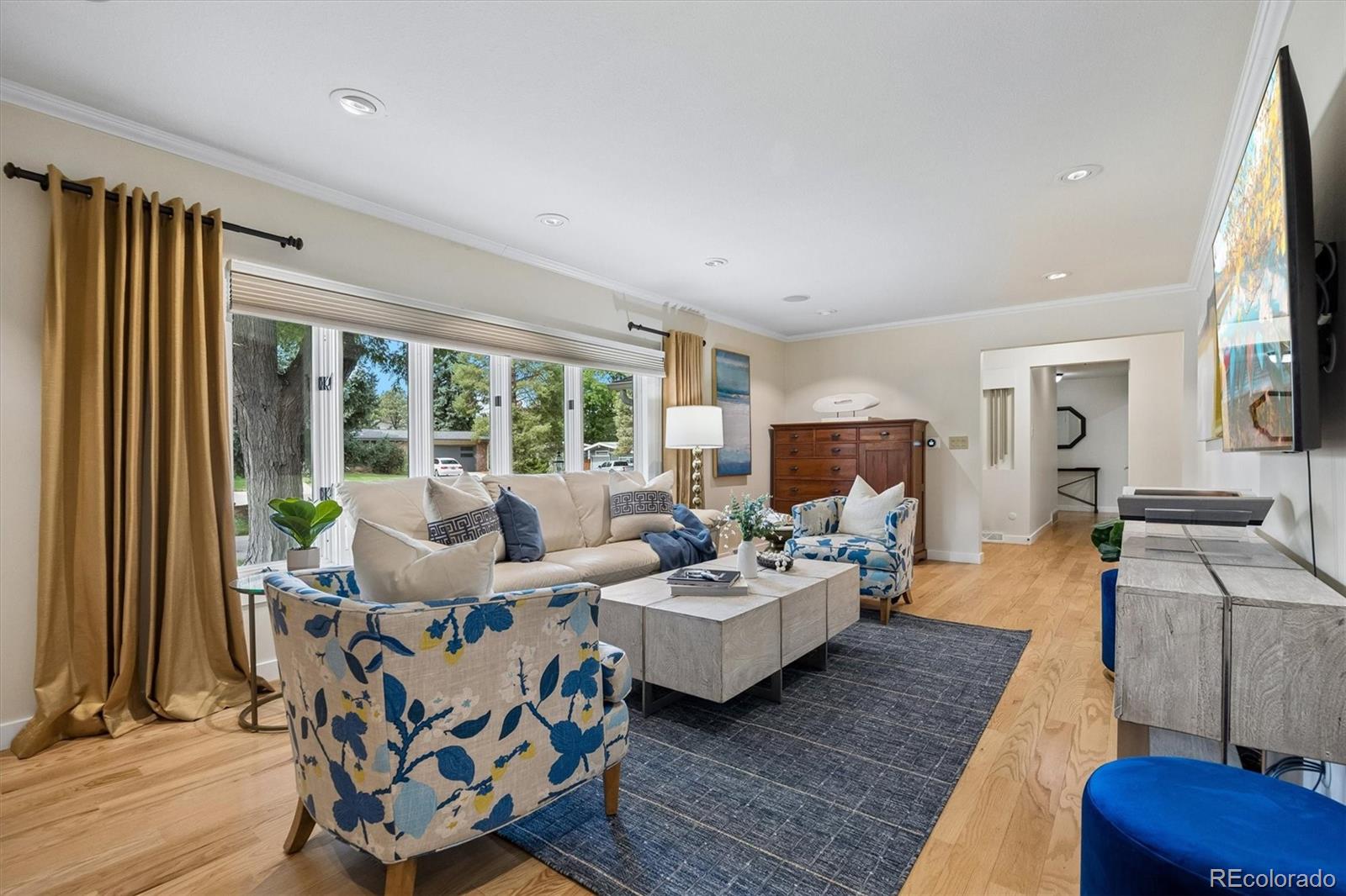 Living room with large windows, gold curtains, blue-patterned armchairs, and light hardwood floors.