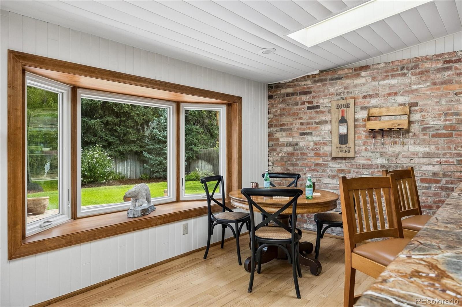 Dining nook with a round table, exposed brick wall, and large wood-trimmed window overlooking the yard.