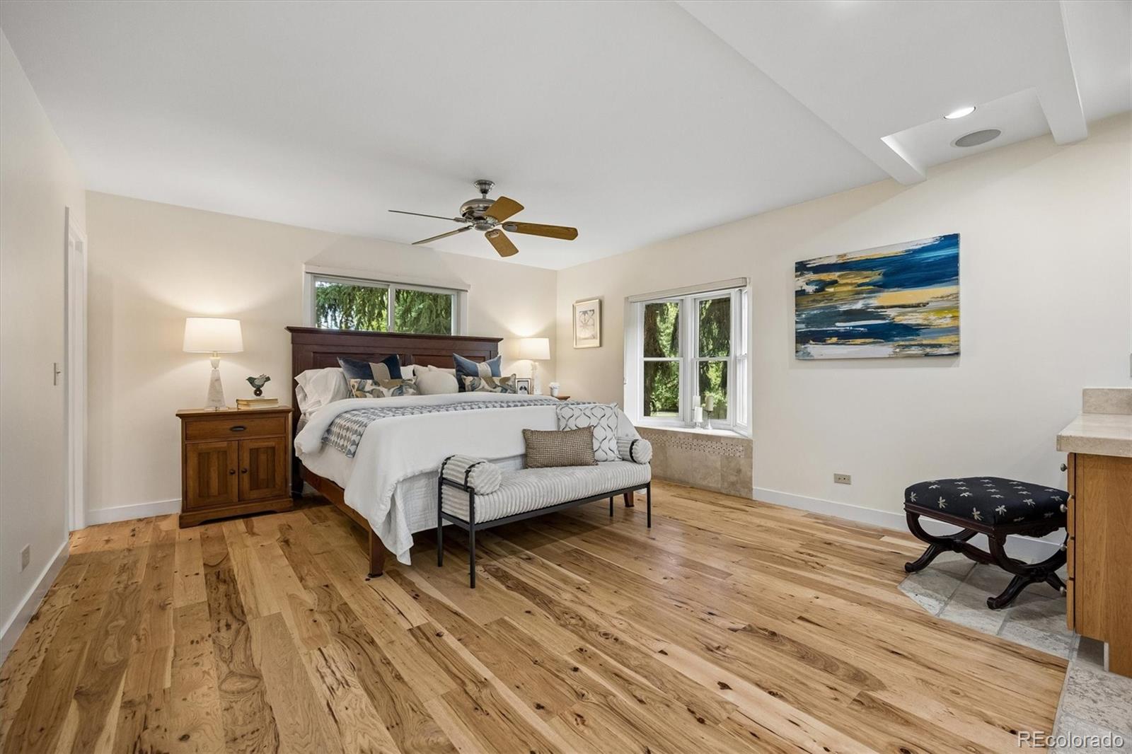 Bedroom with a large bed, striped bench, and warm-toned hardwood floors.