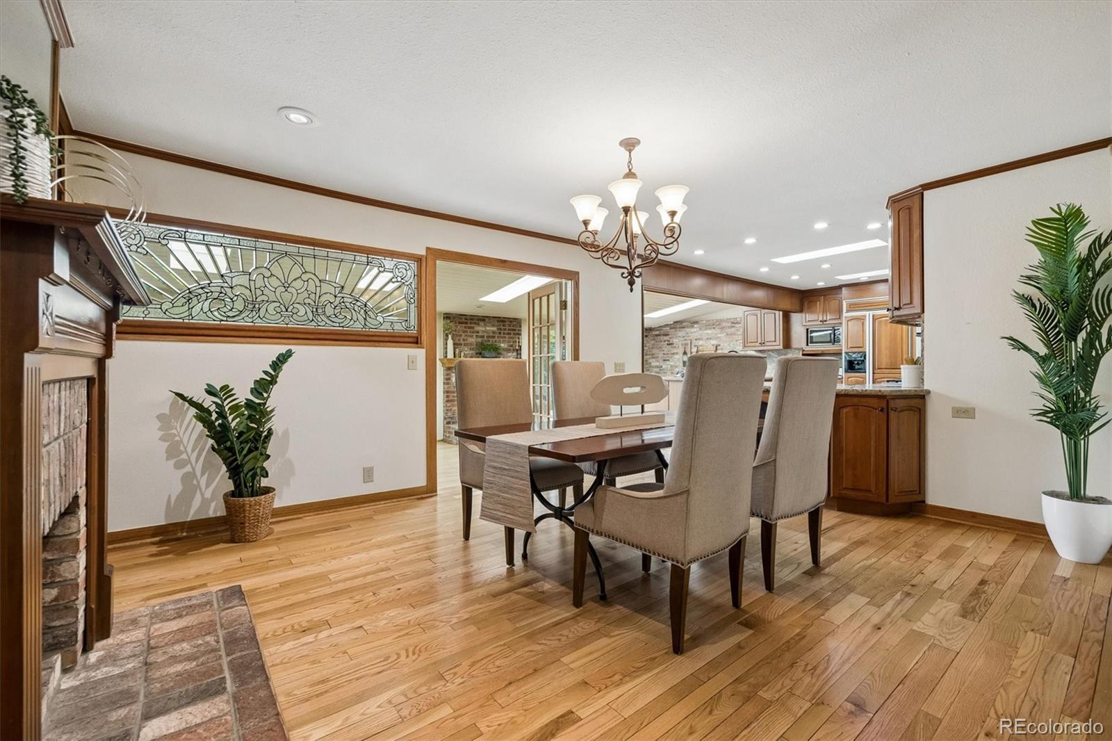 Dining room with hardwood floors, upholstered chairs, a brick fireplace, and an adjoining kitchen.
