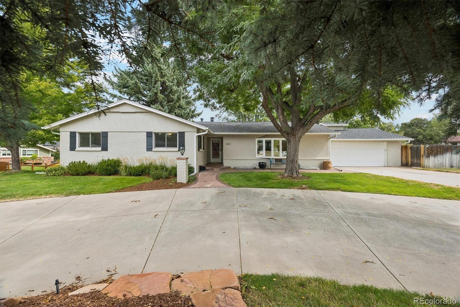 Single-story brick-and-stucco house with a two-car garage and mature trees shading the front yard.