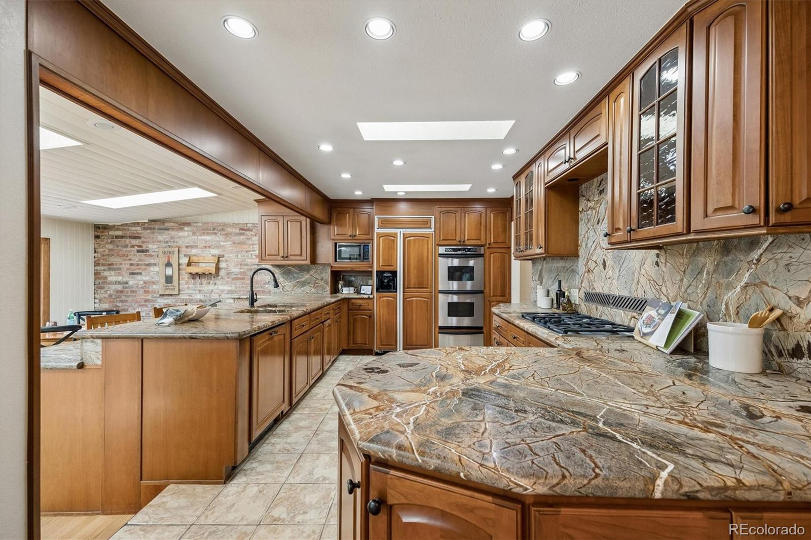 Kitchen with warm wood cabinets, patterned stone counters, a large island, and double wall ovens.