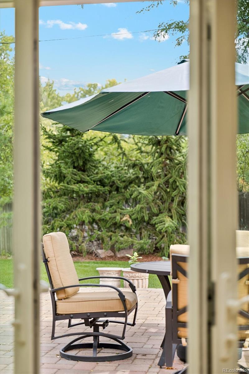 Patio with cushioned chairs and a shade umbrella, viewed through open glass doors.