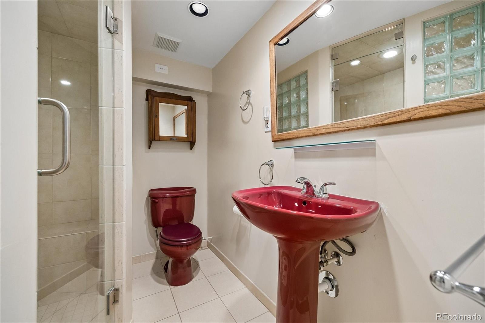 Bathroom with a red pedestal sink and matching toilet beside a glass-enclosed tiled shower.