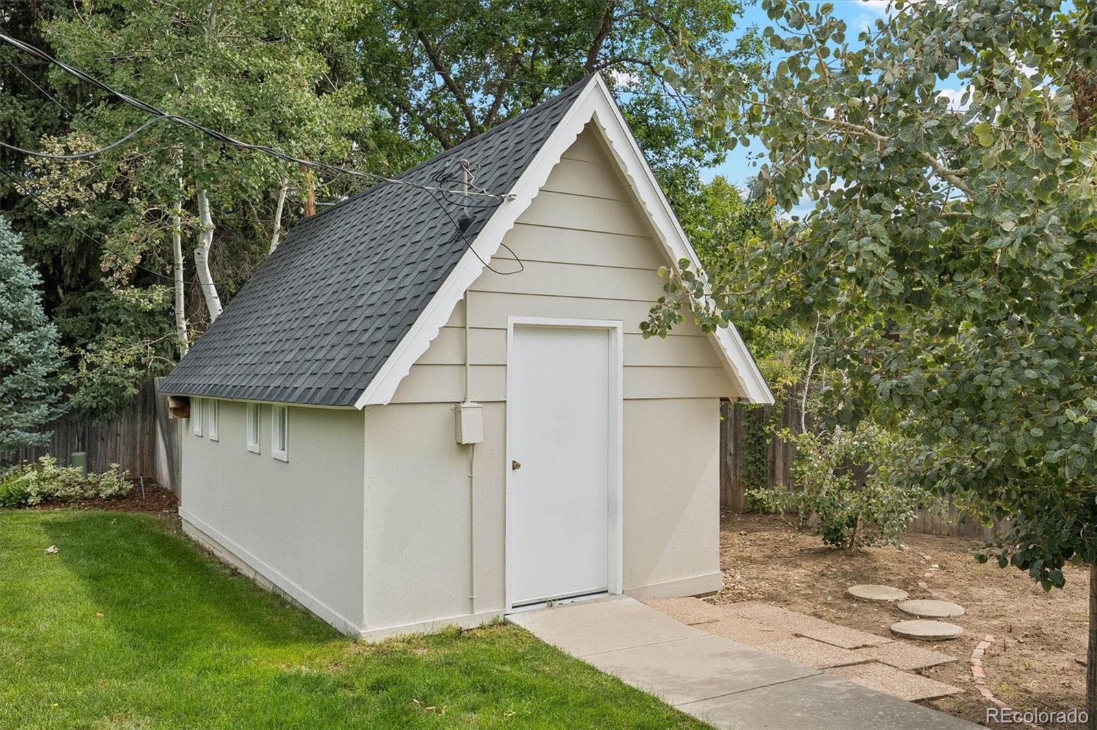 White backyard shed with a steep dark shingle roof and concrete walkway.