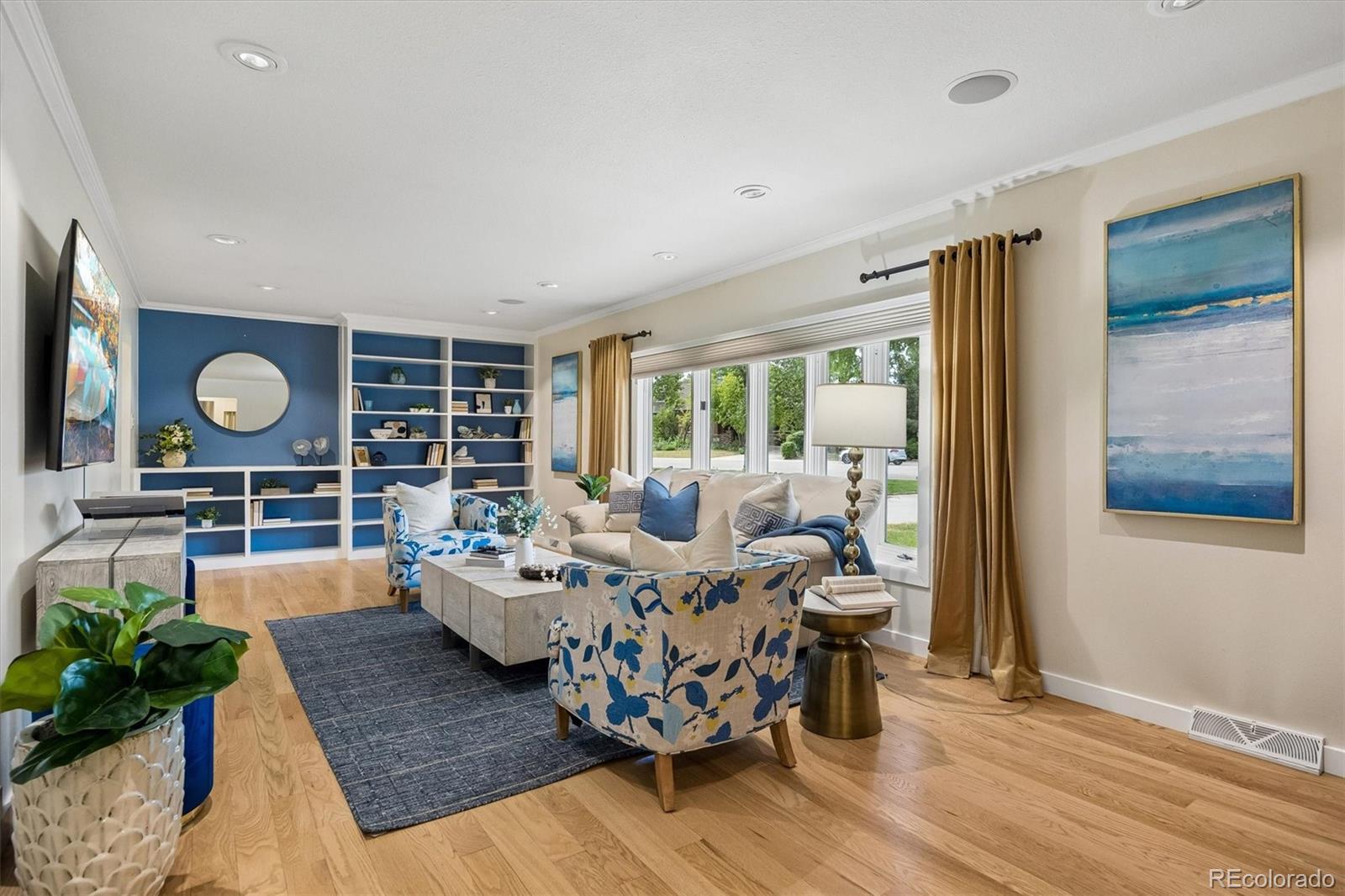 Living room with blue built-in shelves, floral armchairs, and large curtained windows.