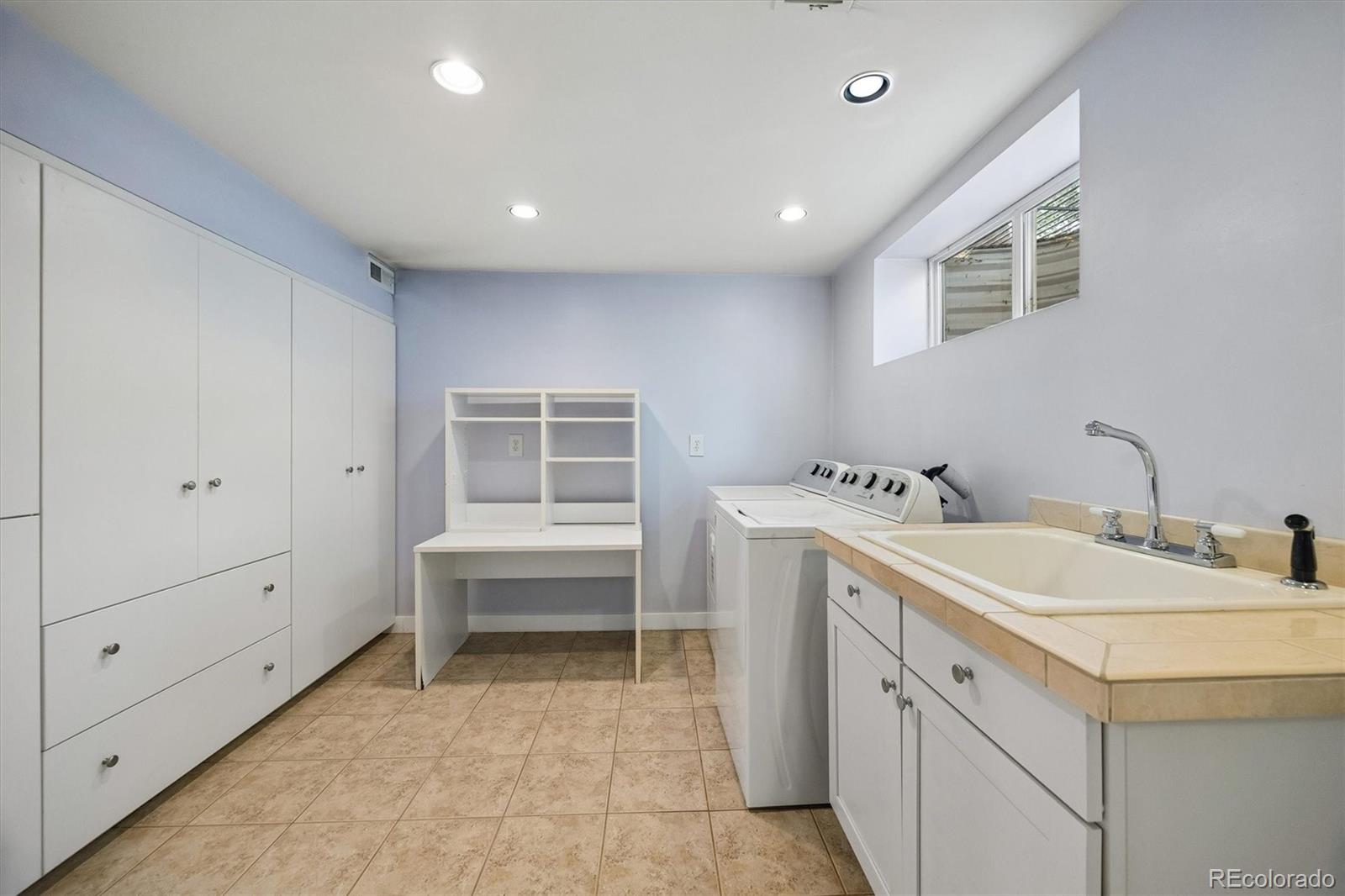Laundry room with white cabinetry, washer and dryer, utility sink, and tiled floor.