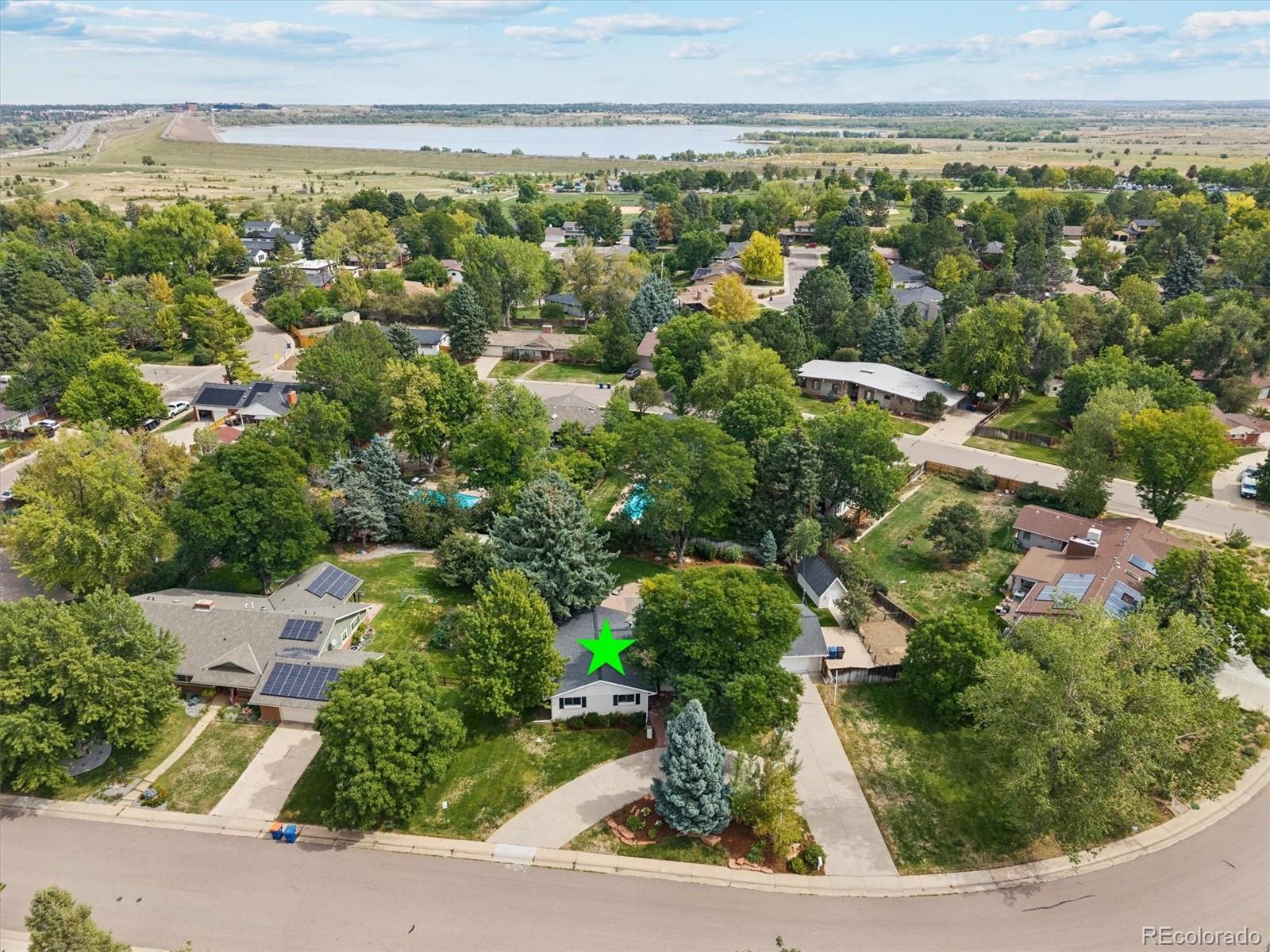Aerial view of the star-marked home, tree-lined neighborhood, and reservoir beyond.