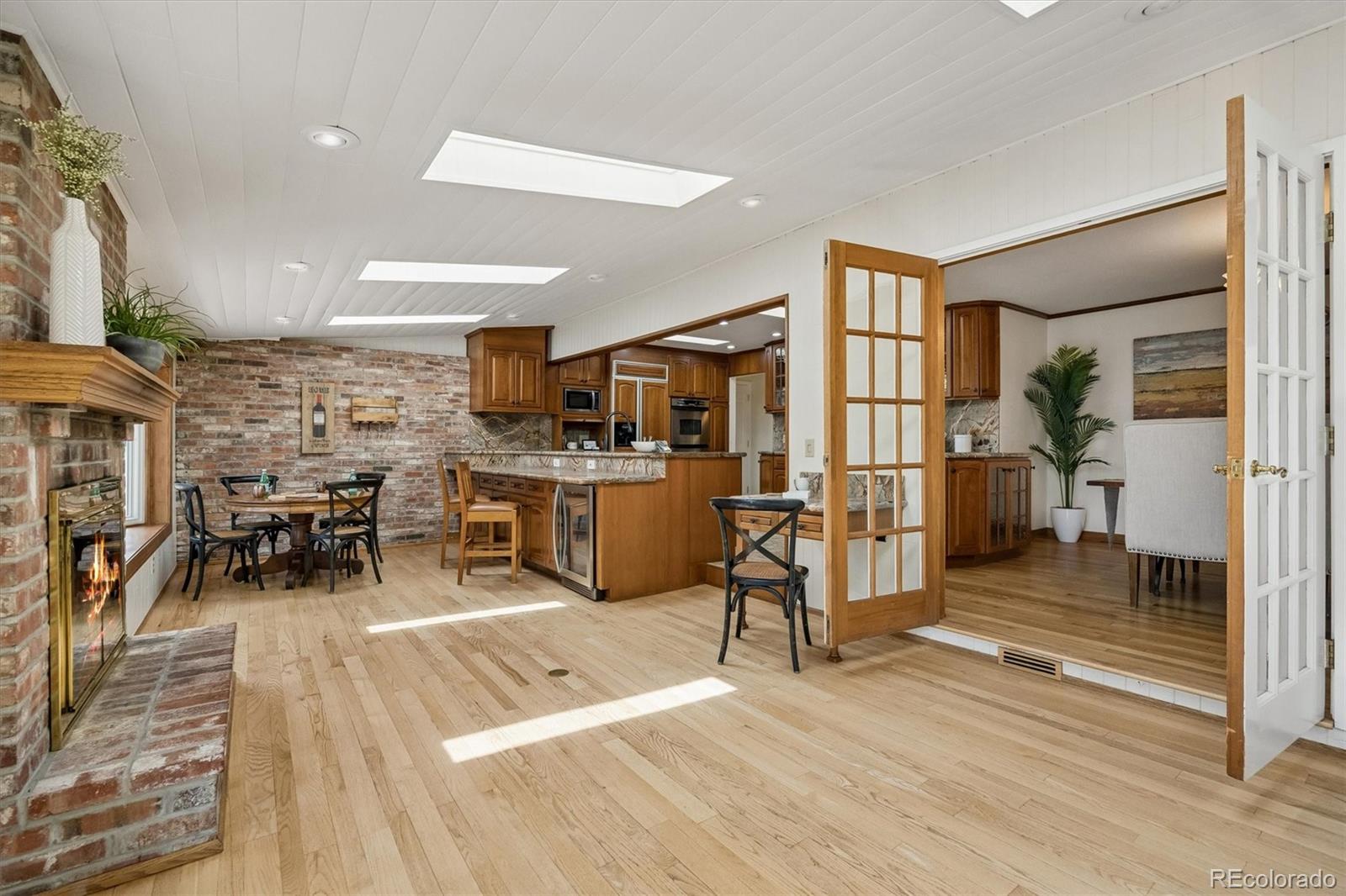 Open kitchen and dining area with wood cabinets, brick fireplace, skylights, and French doors.