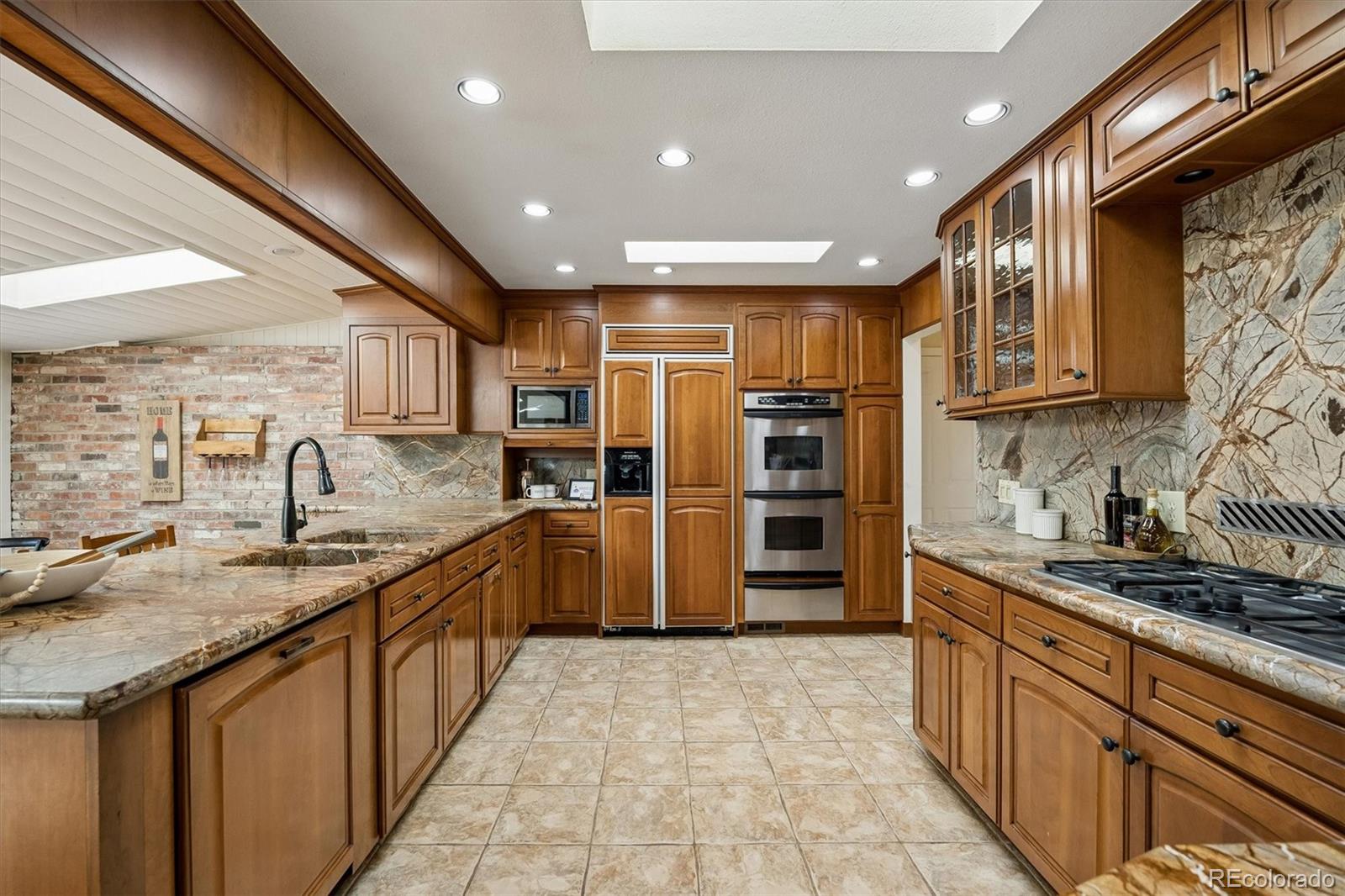Kitchen with warm wood cabinetry, stone counters, double wall oven, and gas cooktop.