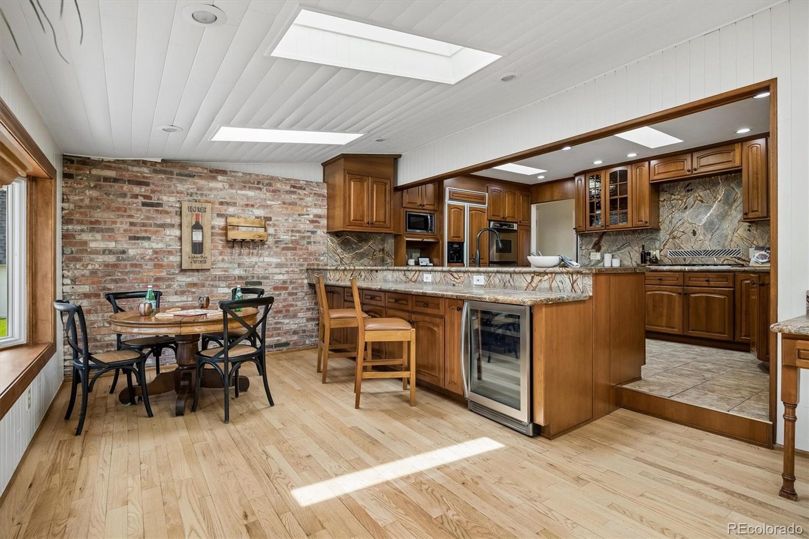 Kitchen with wood cabinets, stone peninsula, skylights, and a dining nook beside an exposed brick wall.