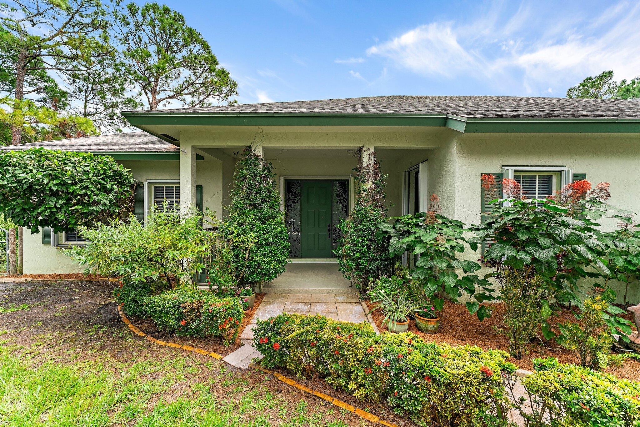 Home entrance with a green front door, covered porch, and landscaped walkway.