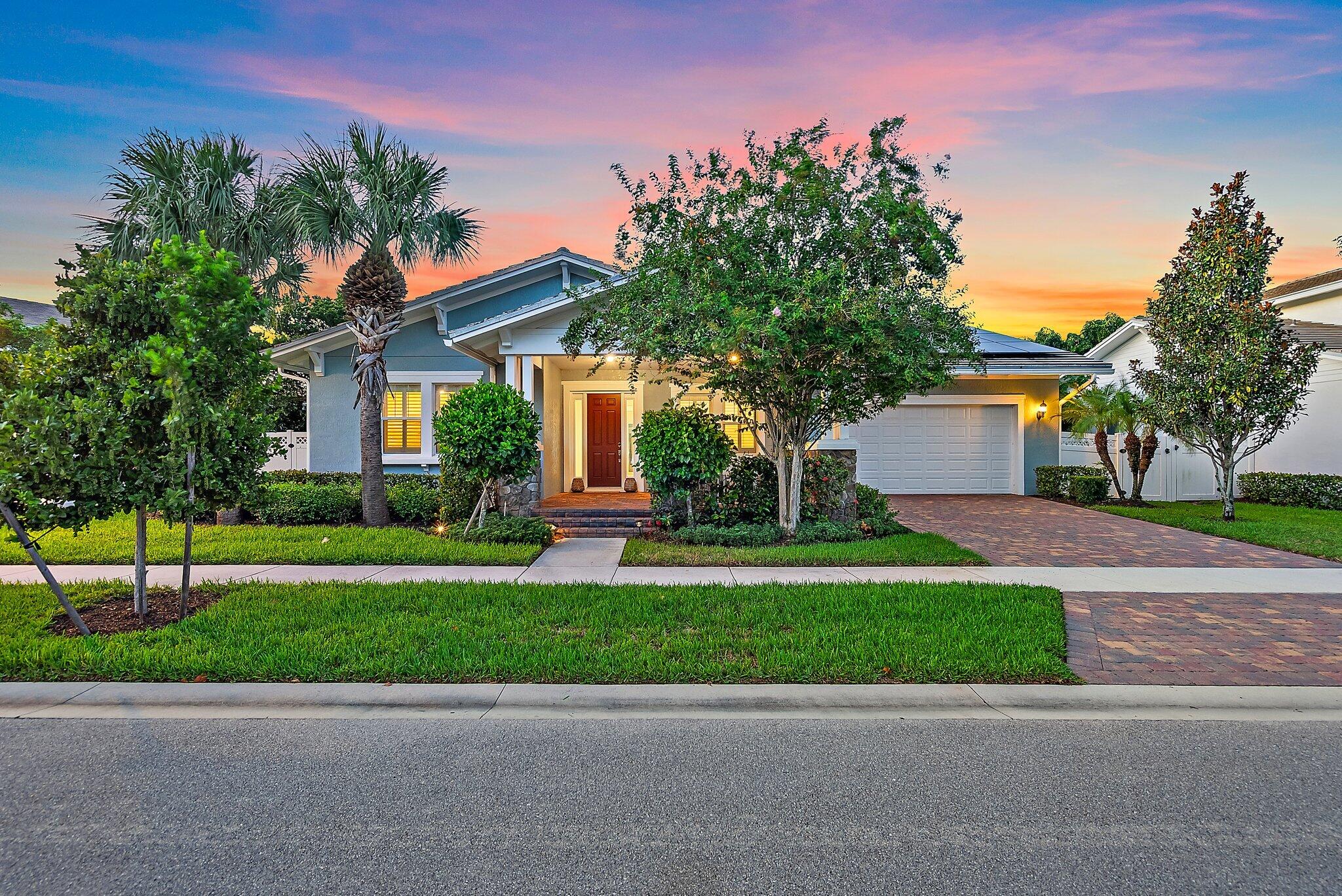 Blue single-story home with an attached garage and landscaped front yard at sunset.