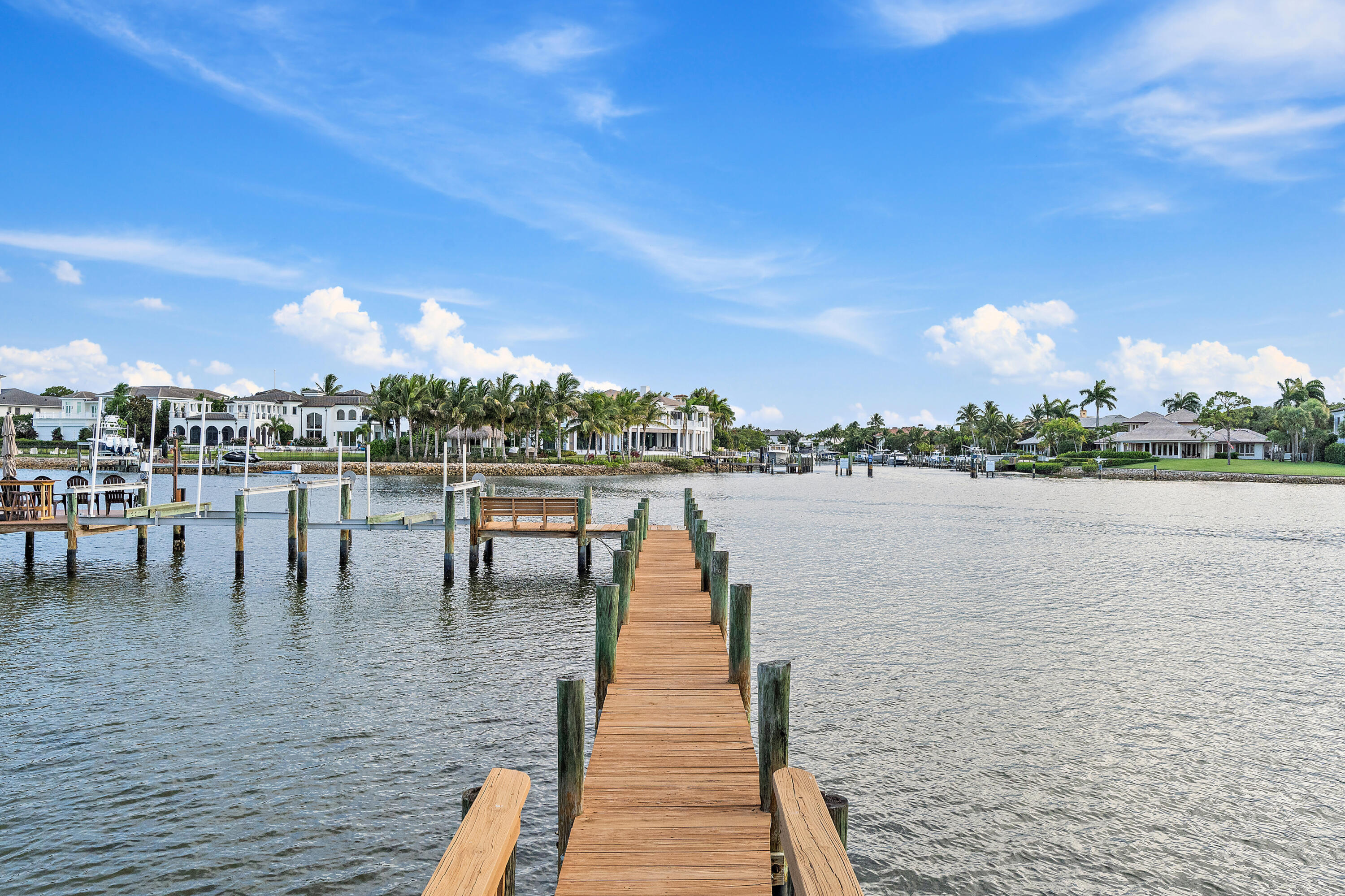 Wooden dock extending toward palm-lined waterfront homes across a broad channel.