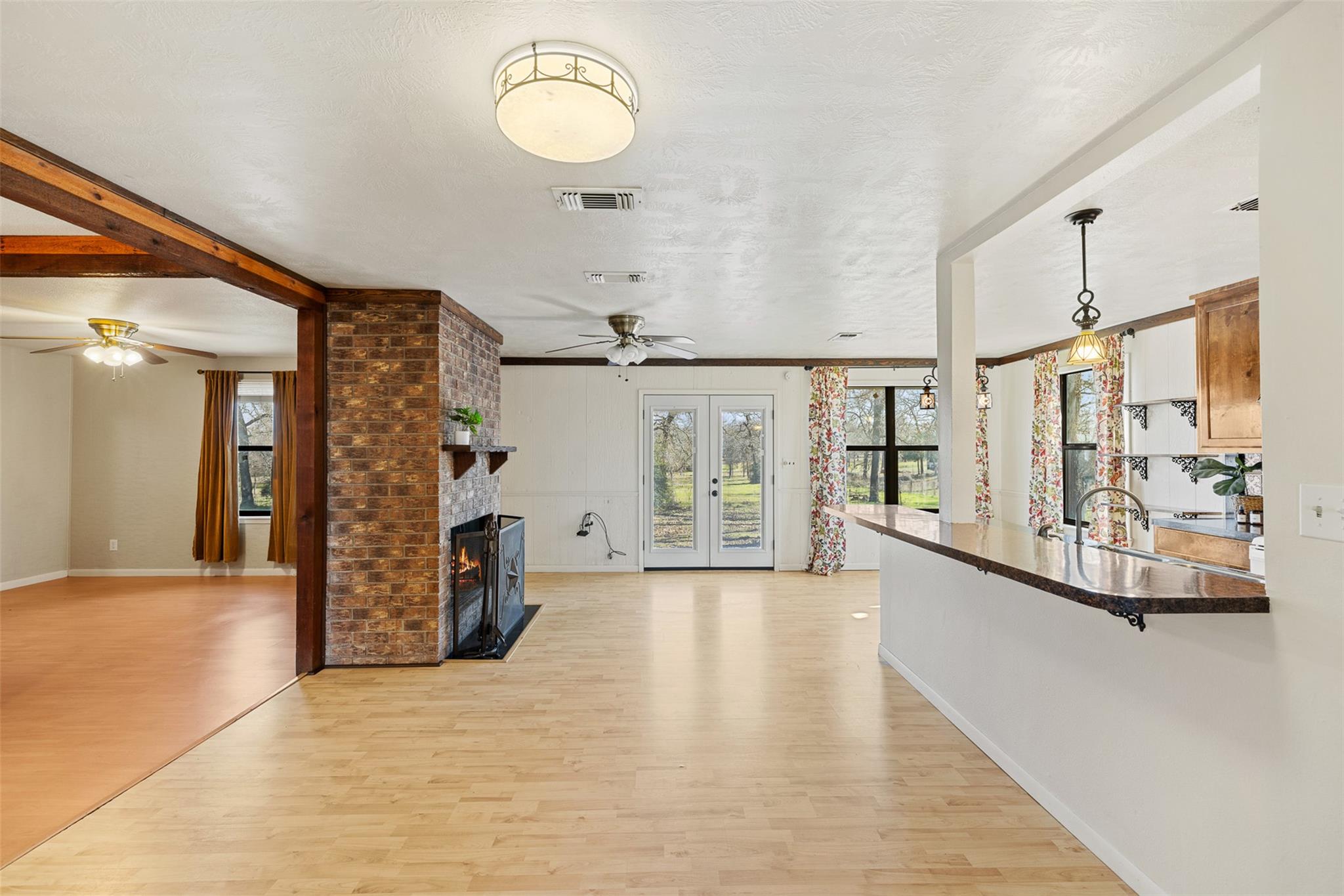 Open-plan living and kitchen area with a brick fireplace, wood flooring, and glass doors to the yard.
