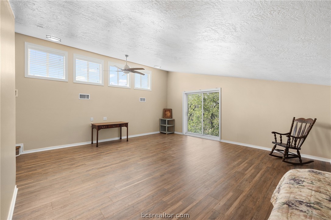 Spacious bedroom with high windows, wood-look flooring, a sliding glass door, and a rocking chair.