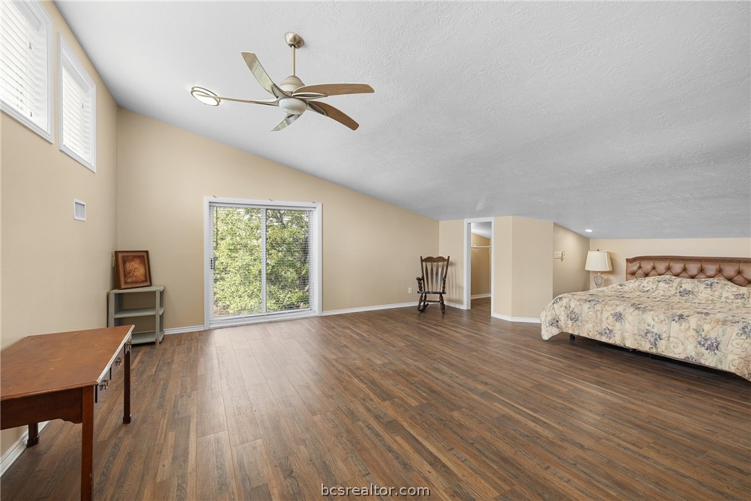 Spacious bedroom with wood-look floors, a ceiling fan, and sliding glass doors overlooking greenery.