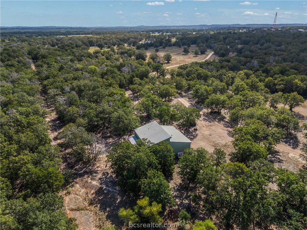 Aerial view of wooded acreage with a small green metal building and cleared dirt tracks.