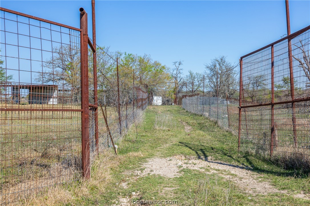 Grassy access lane through open metal gates, with wire fencing and a small outbuilding.