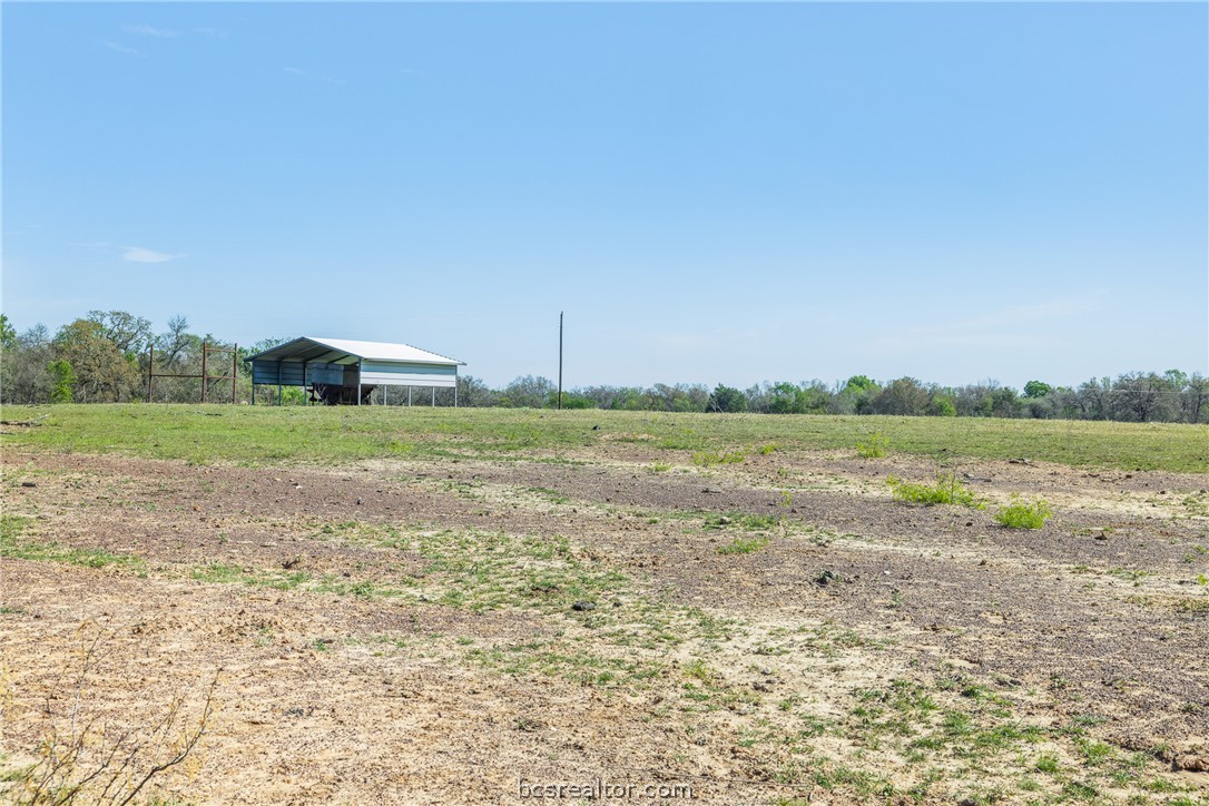 Open rural land with patchy grass and a metal-roofed shelter near the tree line.