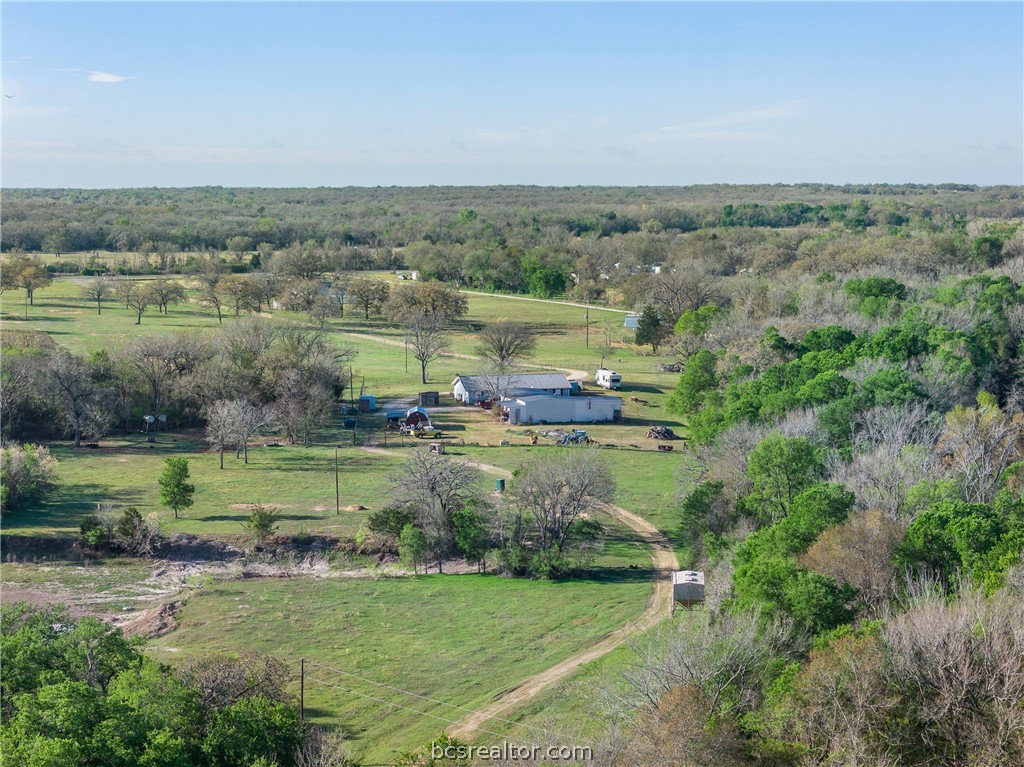 Aerial view of a rural property with grassy acreage, scattered trees, and several outbuildings.