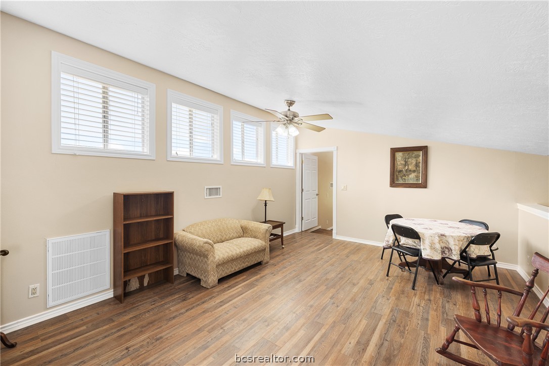 Living and dining area with high windows, wood-look flooring, and a small sofa.