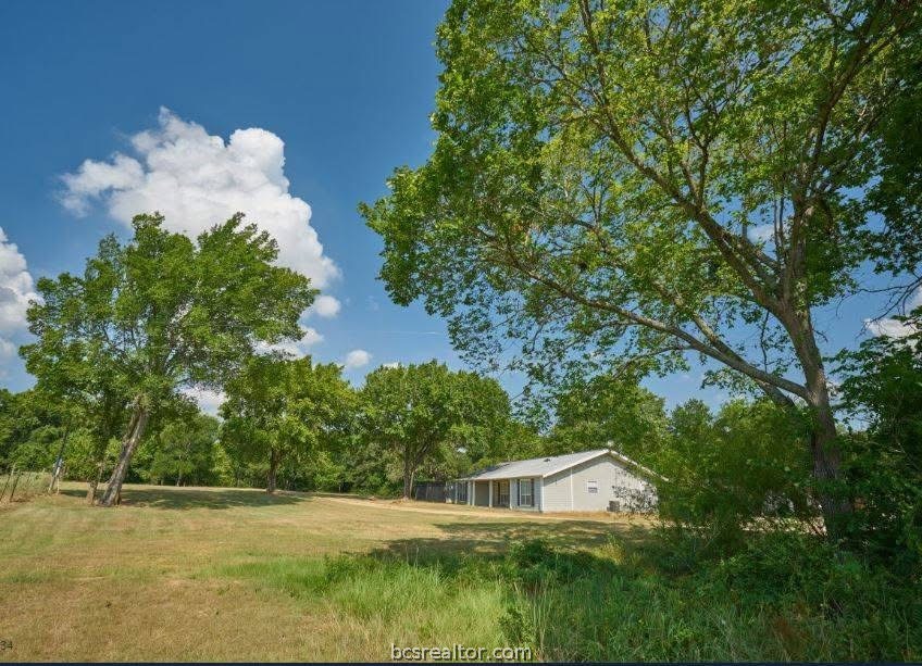Single-story house set back in a grassy yard beneath mature trees.