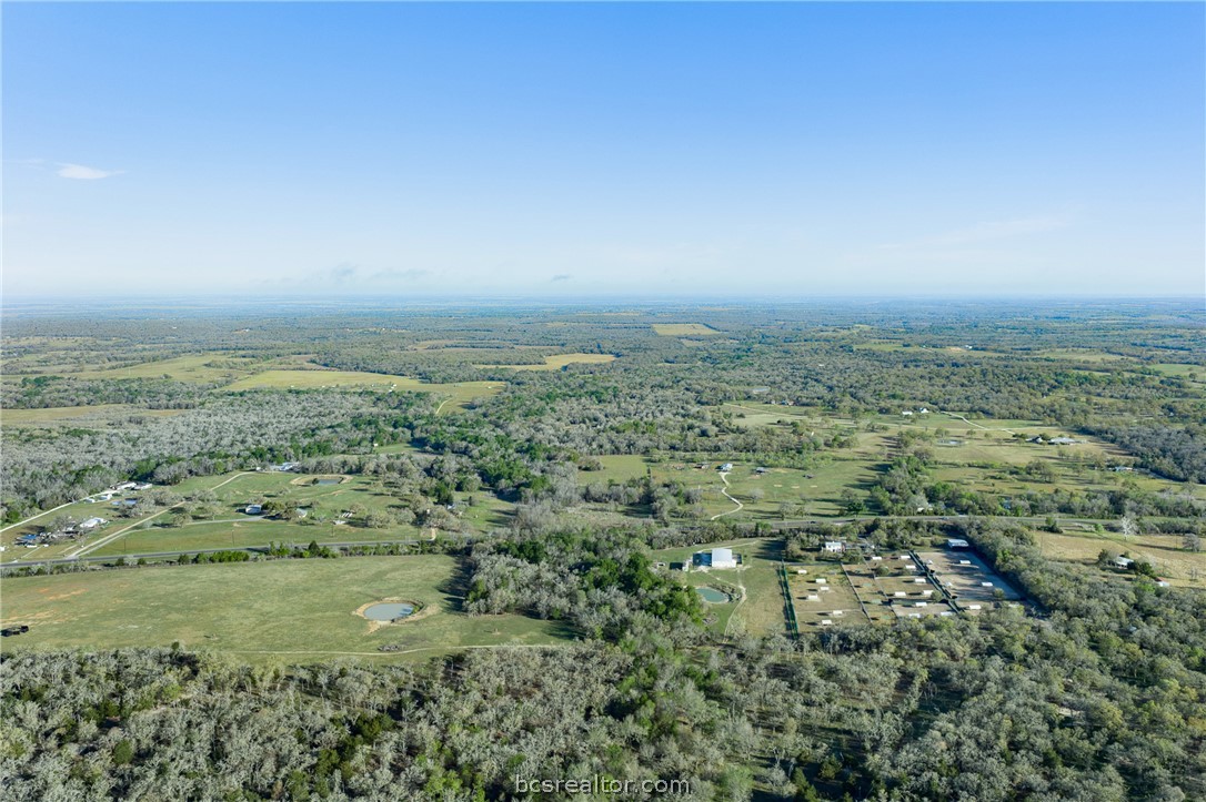 Aerial view of rural acreage with pasture, a small pond, wooded areas, and scattered buildings.