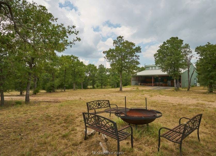 Tree-lined property with a metal barn and a fire pit surrounded by benches.